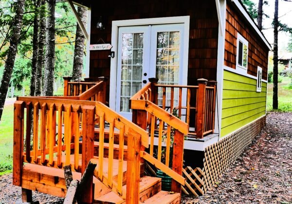 Small timber tiny house with cedar shingles and wooden porch among trees